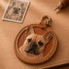 Custom dog portrait leather charm on a leather work surface with a pet photo reference and hand tool, showing the handmade personalization process
