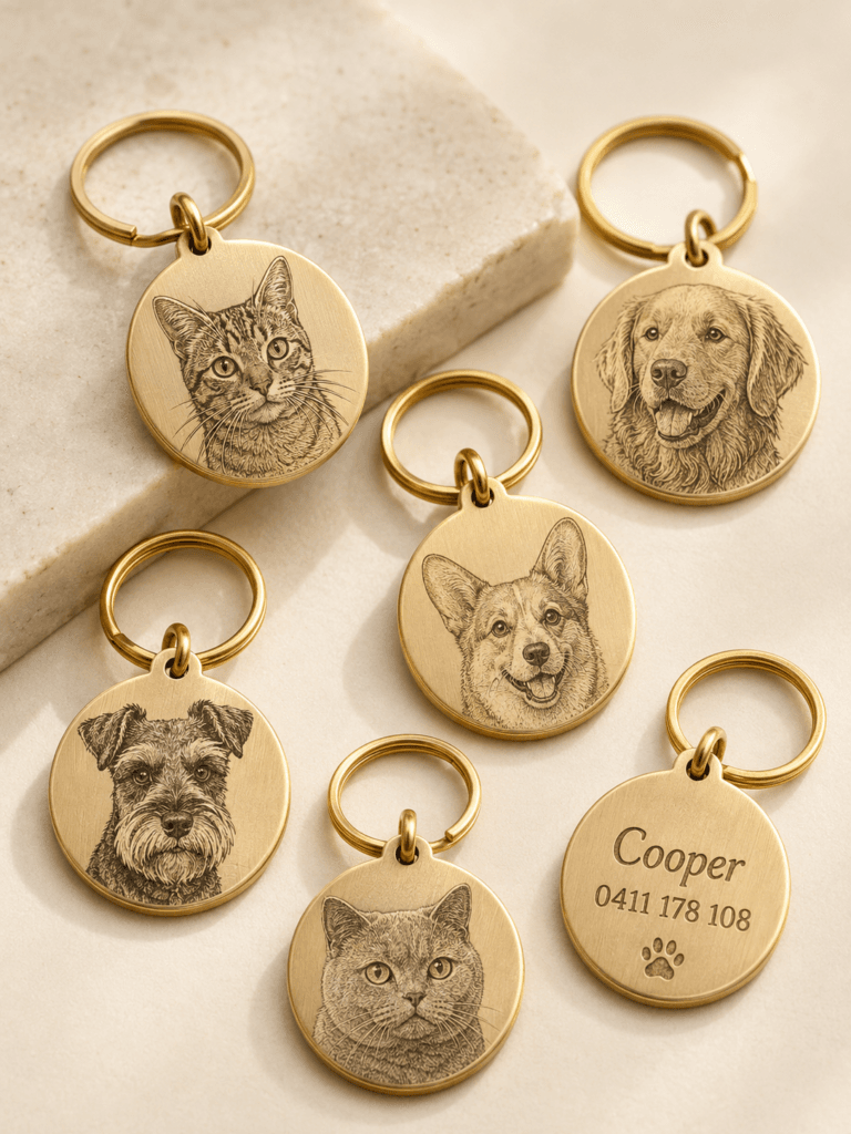 Collection of custom engraved brass pet tags featuring detailed dog and cat portrait engravings, gold keyrings, and personalized name and phone details