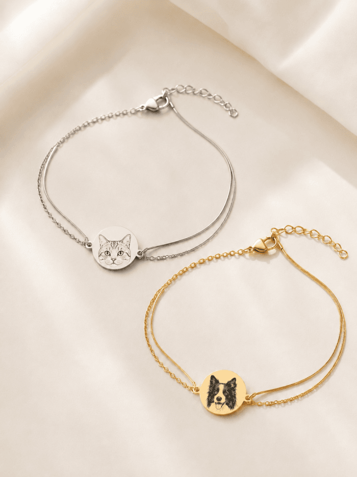 Gold and silver personalized pet portrait bracelets displayed on soft ivory fabric